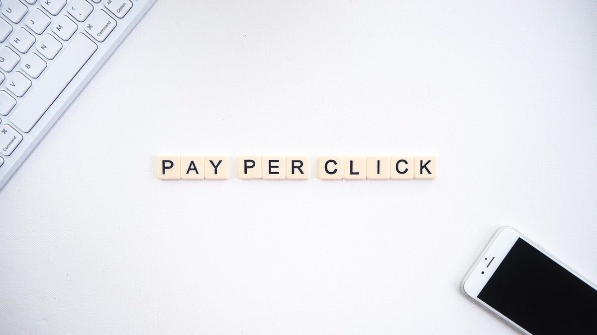 tile letters on white desk spelling out ‘pay per click’ positioned near a smartphone and keyboard